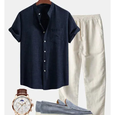 Man wearing a blue slim-fit stand collar short-sleeved shirt and trousers from a coordinated set with shoes and watch.
