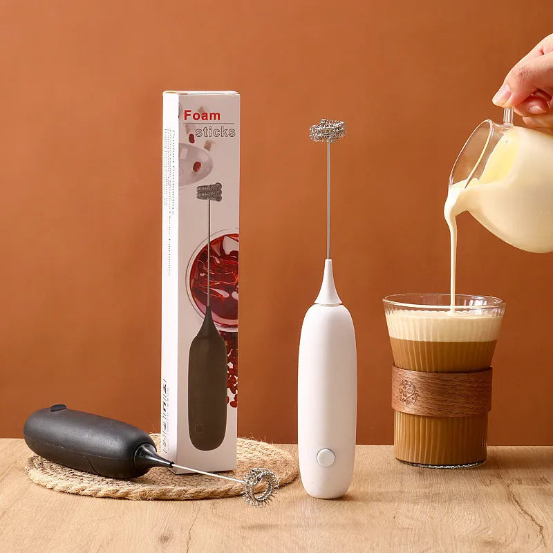 Hand-held milk frother with stainless steel whisk in modern black design creating microfoam in coffee cup