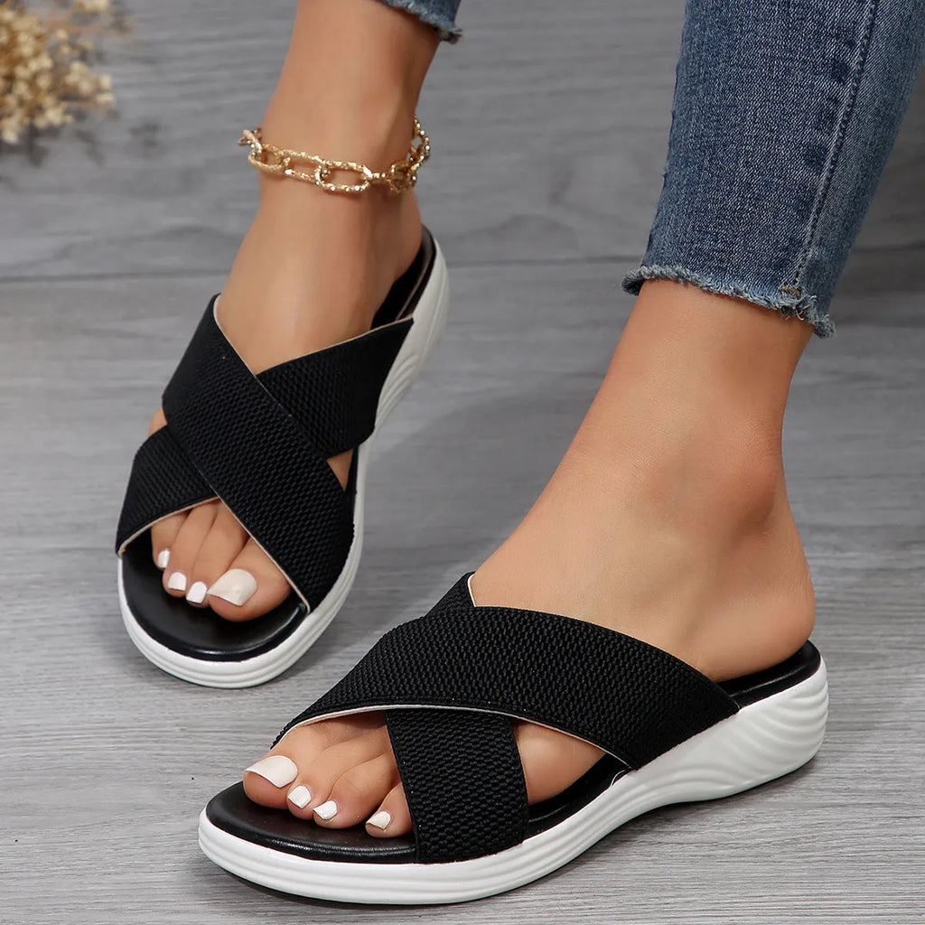 Black women's flat wedge peep-toe slippers with a cross strap and thick rubber sole.