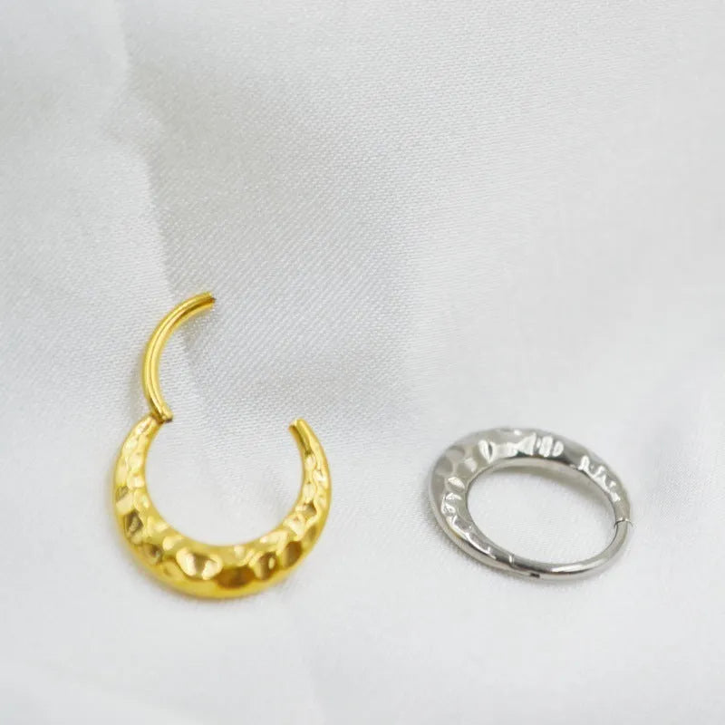 Titanium alloy concave-convex carved nose ring in gold and silver colours on a plain background.