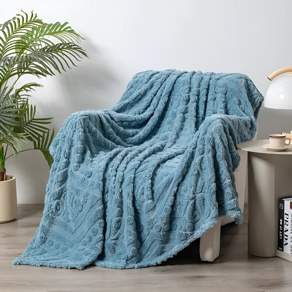 Shu cotton velvet jacquard blanket in fog blue with a plant flower pattern, laid over a grey sofa.