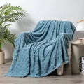 Shu cotton velvet jacquard blanket in fog blue with a plant flower pattern, laid over a grey sofa.