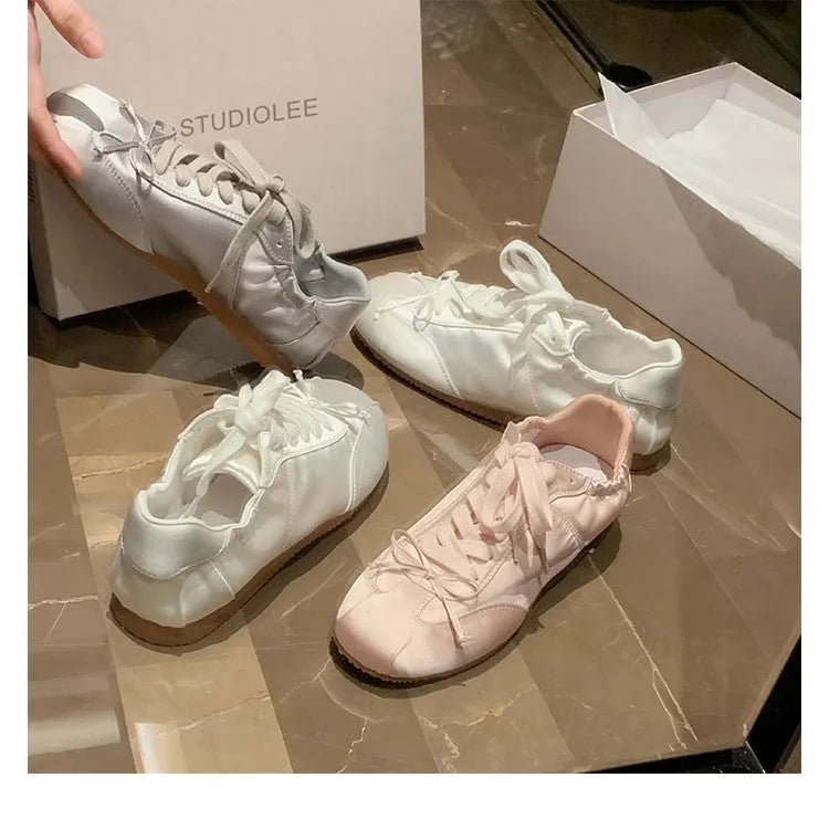 Women's silver grey satin ballet flat with front lace-up fastening and a round toe, shown on a white background.
