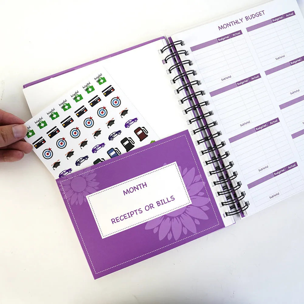 Purple coil-bound financial planning notebook open on a monthly budget page with pen and stickers.