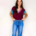 Burgundy loose V-neck sweater with cuffed short sleeves and light contrast trim laid flat.