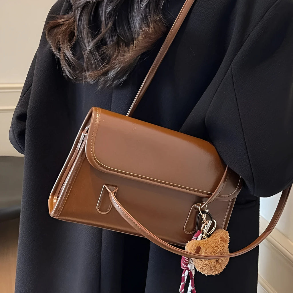 Brown women's structured shoulder bag with horizontal square shape, pendant accessory, and double joint shoulder straps