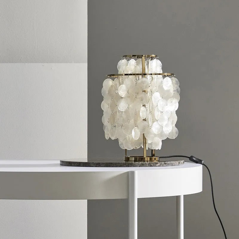 Modern shell-shaped bedside table lamp in a chrome finish on a wooden surface.