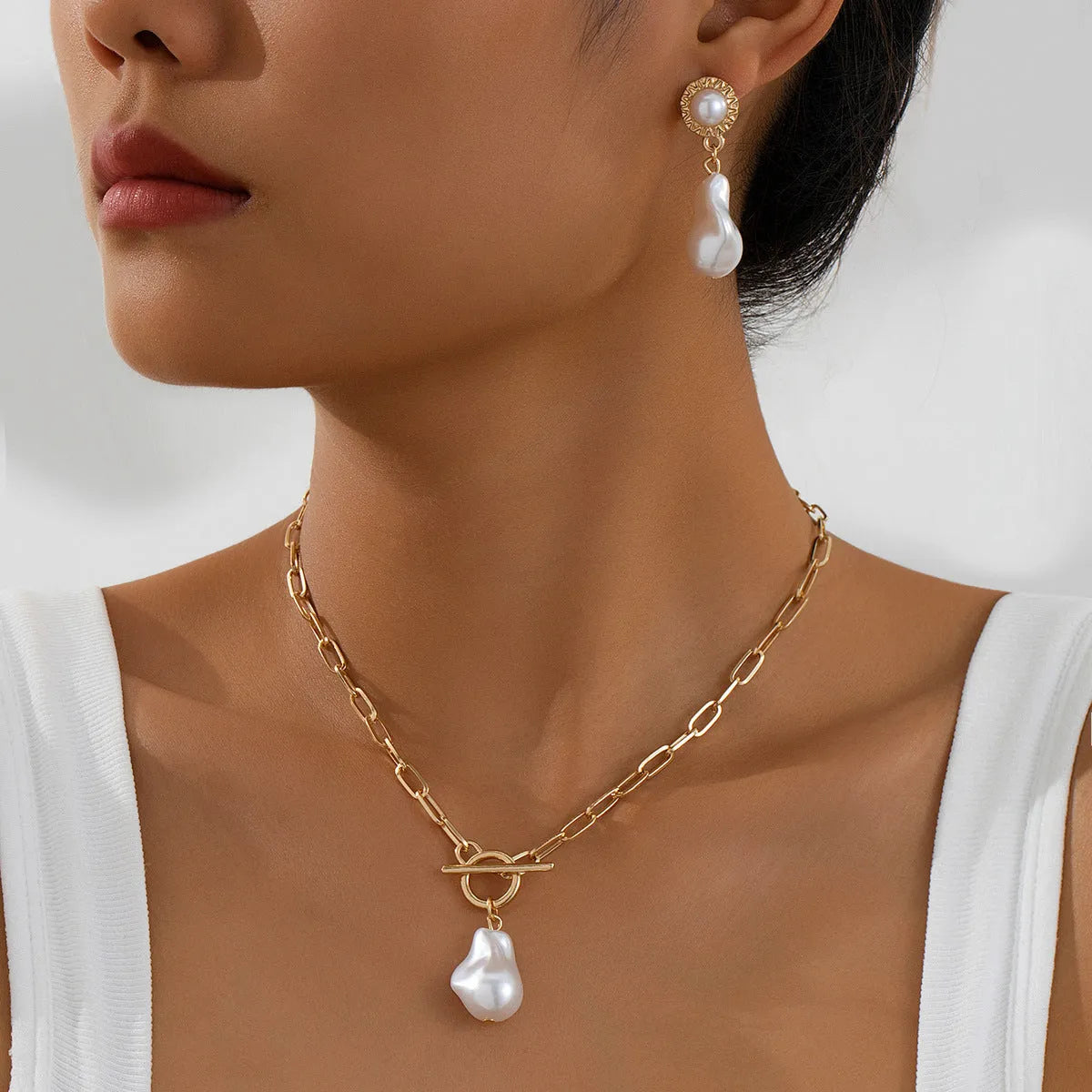 Gold-coloured iron necklace and earrings set with baroque pearl decorative elements on dark background