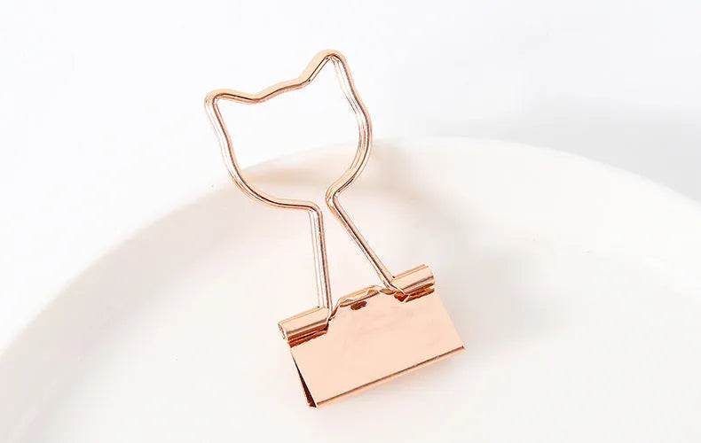 Golden alloy office clip with decorative top, 6.5cm long, holding papers on a desk