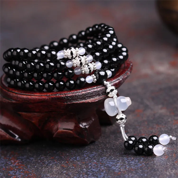 Black agate bracelet with 108 beads and geometric shape on a wrist.