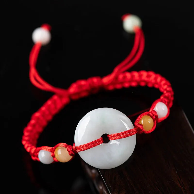 Round emerald green Burma jade pendant on an adjustable red rope bracelet strap.