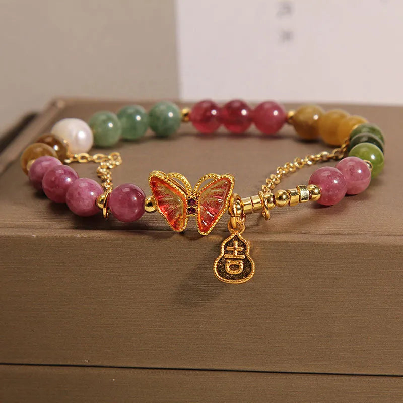 Close-up of a women's agate and tourmaline charm bracelet with butterfly and gourd shapes on a white background.