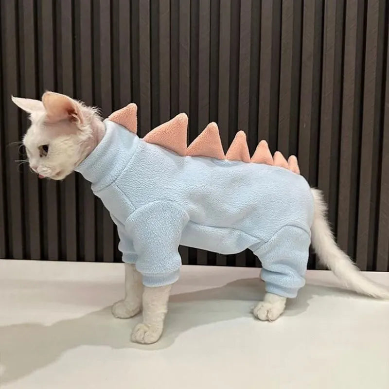 Sphynx cat wearing green dinosaur costume with tail and spikes, showing full-body fleece outfit