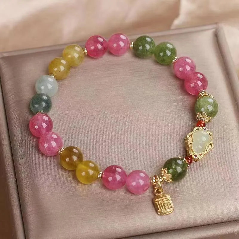 Close-up of a women's bracelet with a colourful tourmaline gourd charm and electroplated floral links.