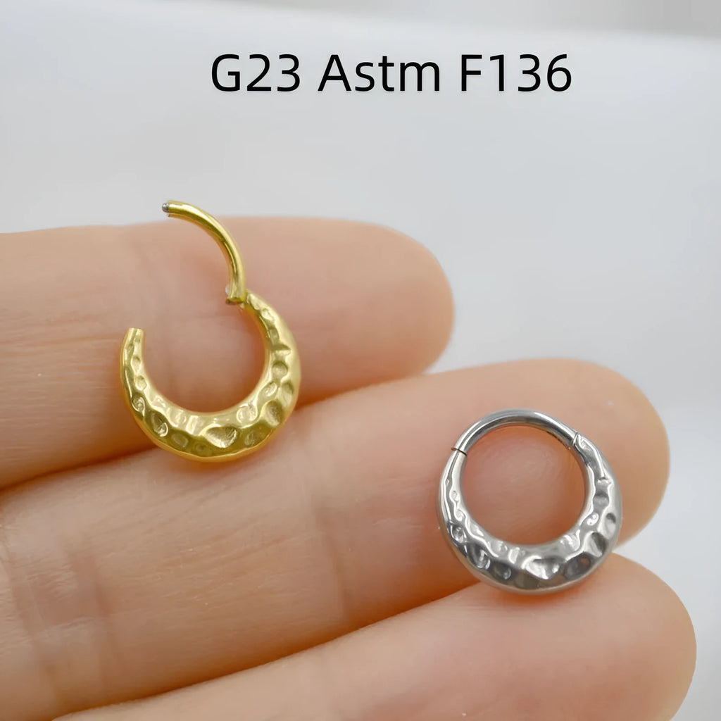 Titanium alloy concave-convex carved nose ring in gold and silver colours on a plain background.