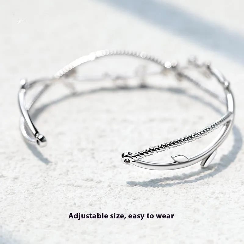Close-up of an adjustable white gold coloured copper bracelet with a twisted branch and sprout design.