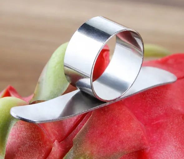 A silver stainless steel finger-ring style citrus peeler for oranges and pomelo on a kitchen surface.