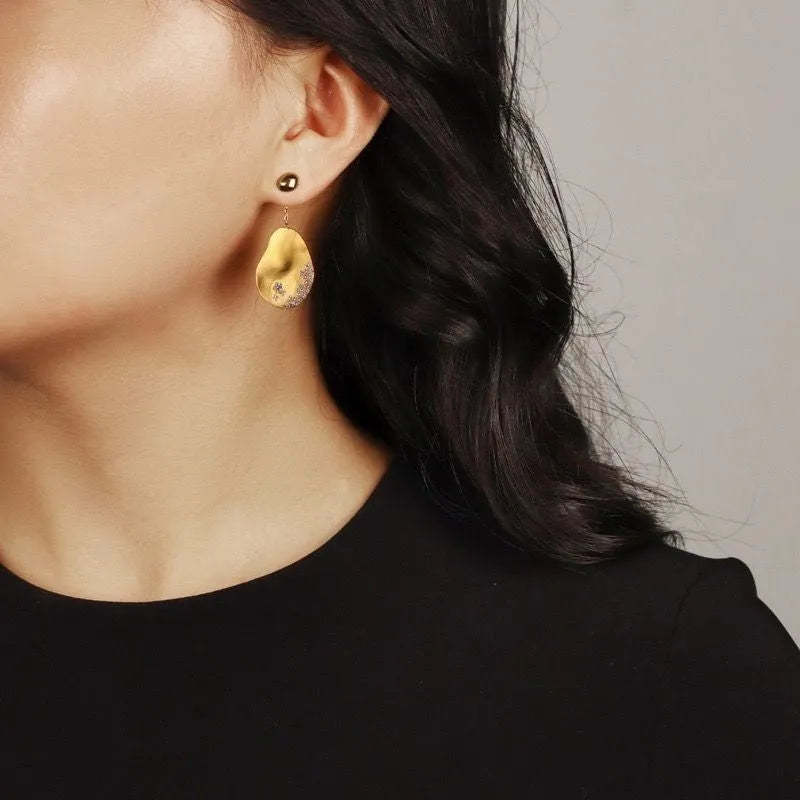 Asymmetric gold and silver floral drop earrings with clear zircon stone detailing on a white background.