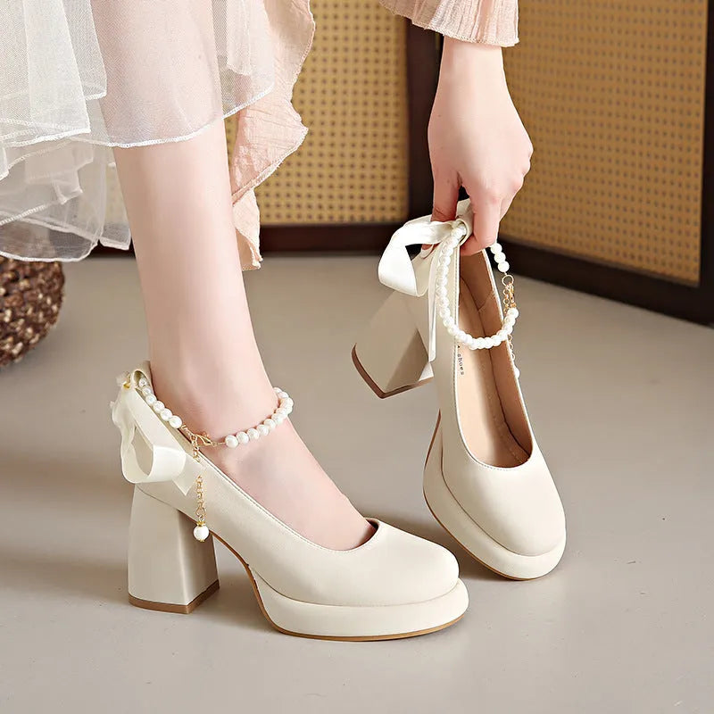 Beige women's Mary Jane shoes with a chunky heel, round toe, and pearl-decorated ankle strap buckle on a white background.