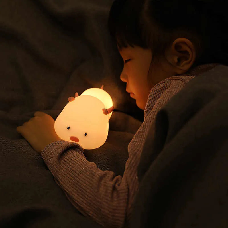 Cute pink silicone pig night light with sleeping design on a bedside table.