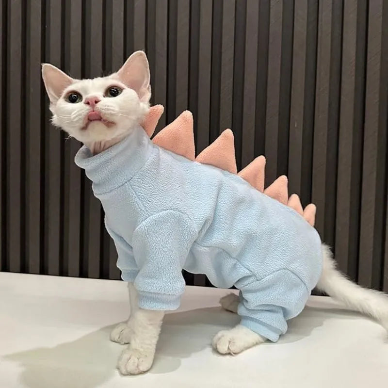 Sphynx cat wearing green dinosaur costume with tail and spikes, showing full-body fleece outfit