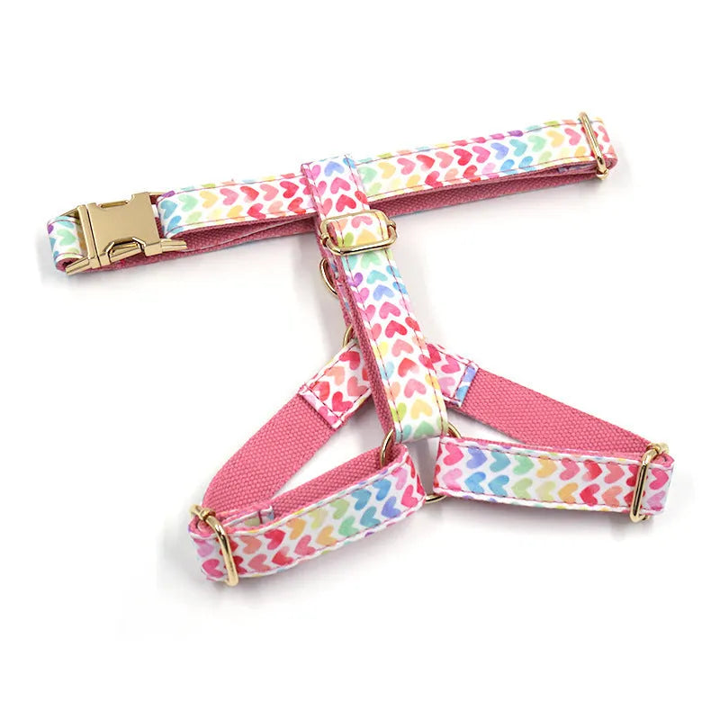 Pink colourful dog harness with heart-shaped stone details and a gold buckle on a white background.