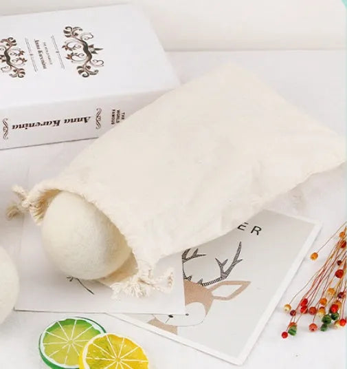 Set of 100% wool anti-static drying balls next to a plain cotton storage bag on a laundry background.