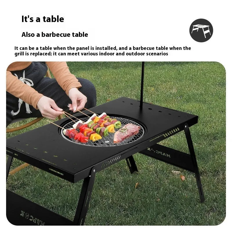 Black folding steel camping table with an integrated barbecue grill set up outdoors.