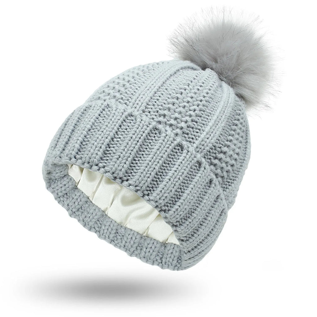 Women's white skull knit beanie with faux fur pom pom, showing satin paisley lining.
