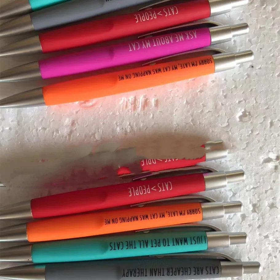 Set of five coloured push-action pens with cat and dog designs next to a beaded storage bag.