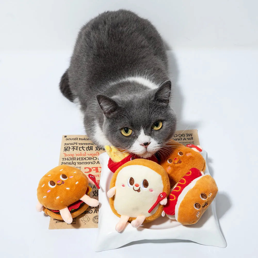 Set of five colourful cat chewing toys shaped like hamburger, chicken legs, fries, hot dog, and bread slice on a white background.