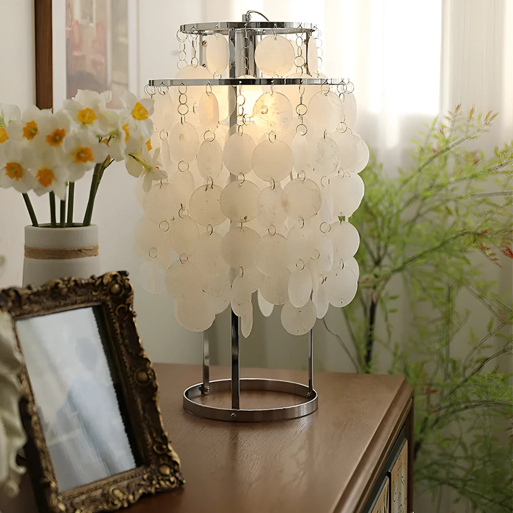 Modern shell-shaped bedside table lamp in a chrome finish on a wooden surface.