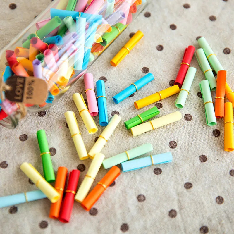Assorted colourful mini paper scrolls with eyelets for drift bottle messages in sizes 3x7cm, 4x7cm, 7x7cm, and 5x5cm.