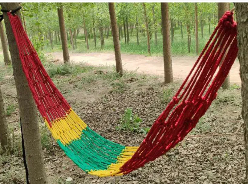 Green nylon rope mesh hammock hung between two trees with tying ropes.