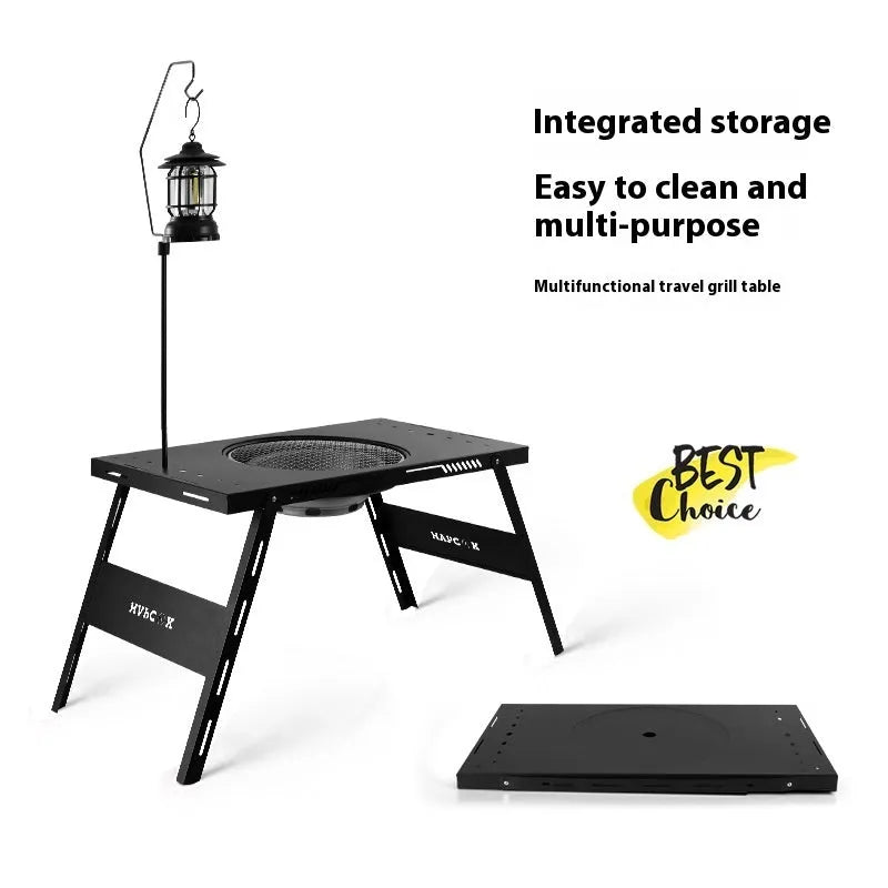 Black folding steel camping table with an integrated barbecue grill set up outdoors.
