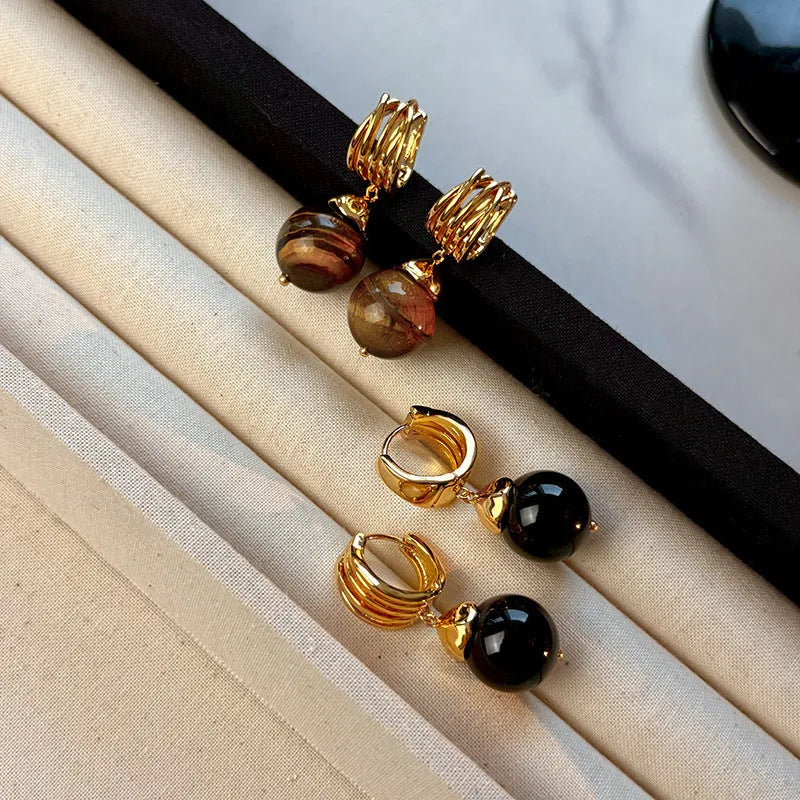 A pair of geometric tigereye stone earrings with 18K gold plating, showing natural brown bands, on a grey background.