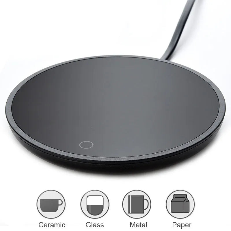 Black coffee cup warmer pad with temperature switch on a desk next to a mug.