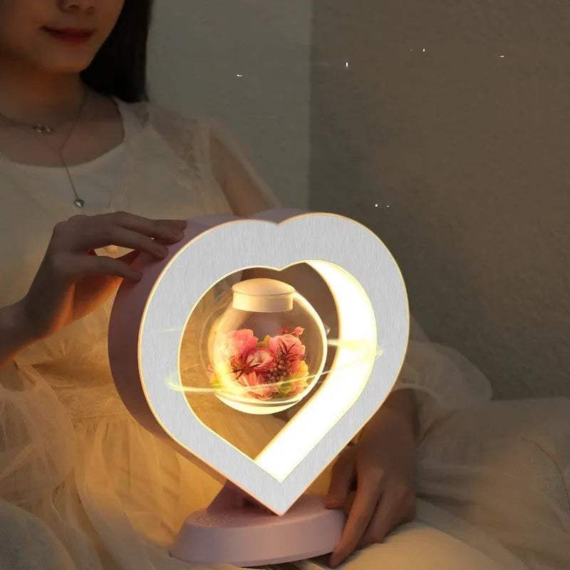 Pink magnetic levitation heart LED night light rotating above a triangular base on a desk.