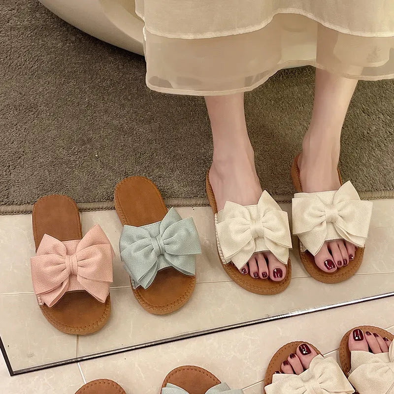 Women's beige suede slip-on sandals with a bow and soft rubber flat sole.