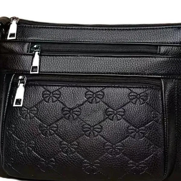 Women's black messenger bag with crossbody strap showing embossed detailing and exterior slit pocket