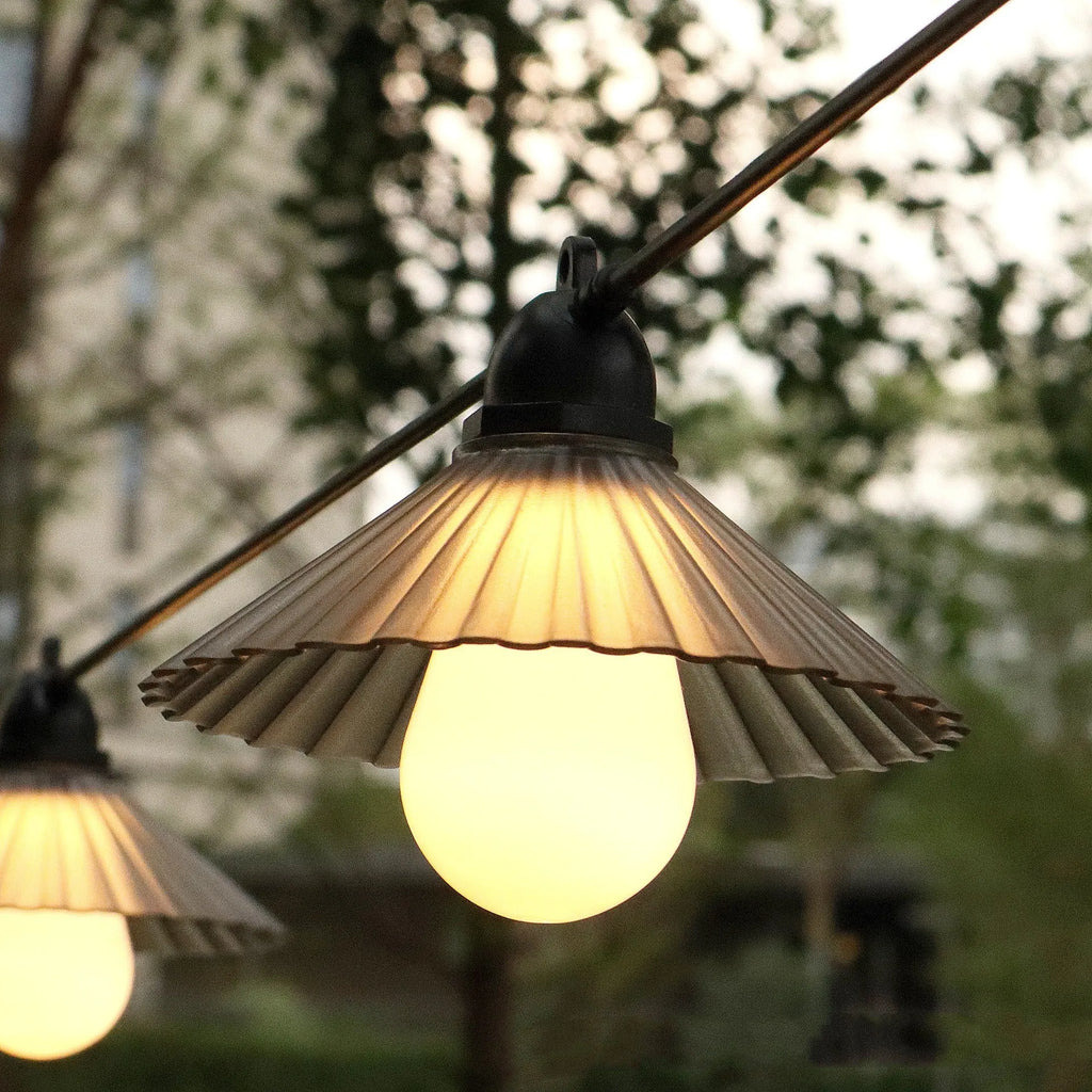 Outdoor LED string lights with white flower-shaped bulbs hanging in a garden setting.
