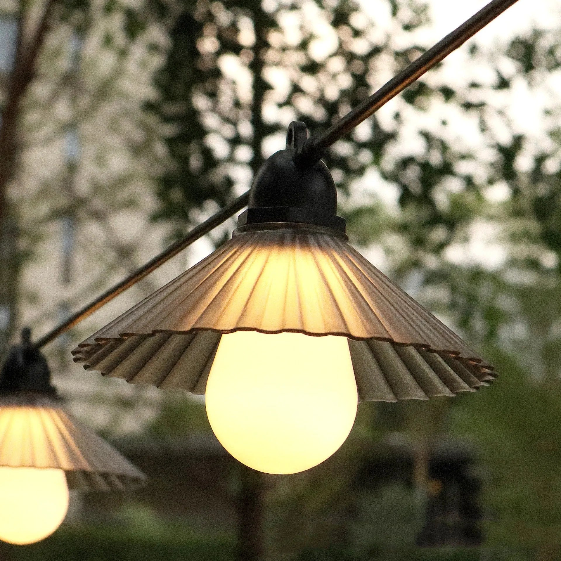 Outdoor LED string lights with white flower-shaped bulbs hanging in a garden setting.