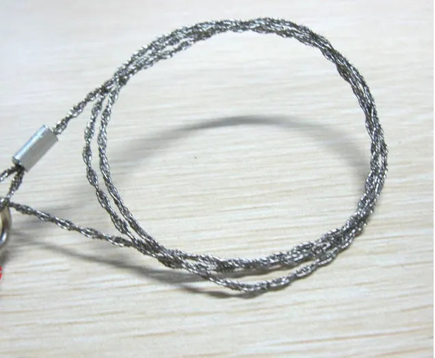 Coiled stainless steel survival wire saw with two black thumb rings, shown next to a ruler showing its 55cm length.
