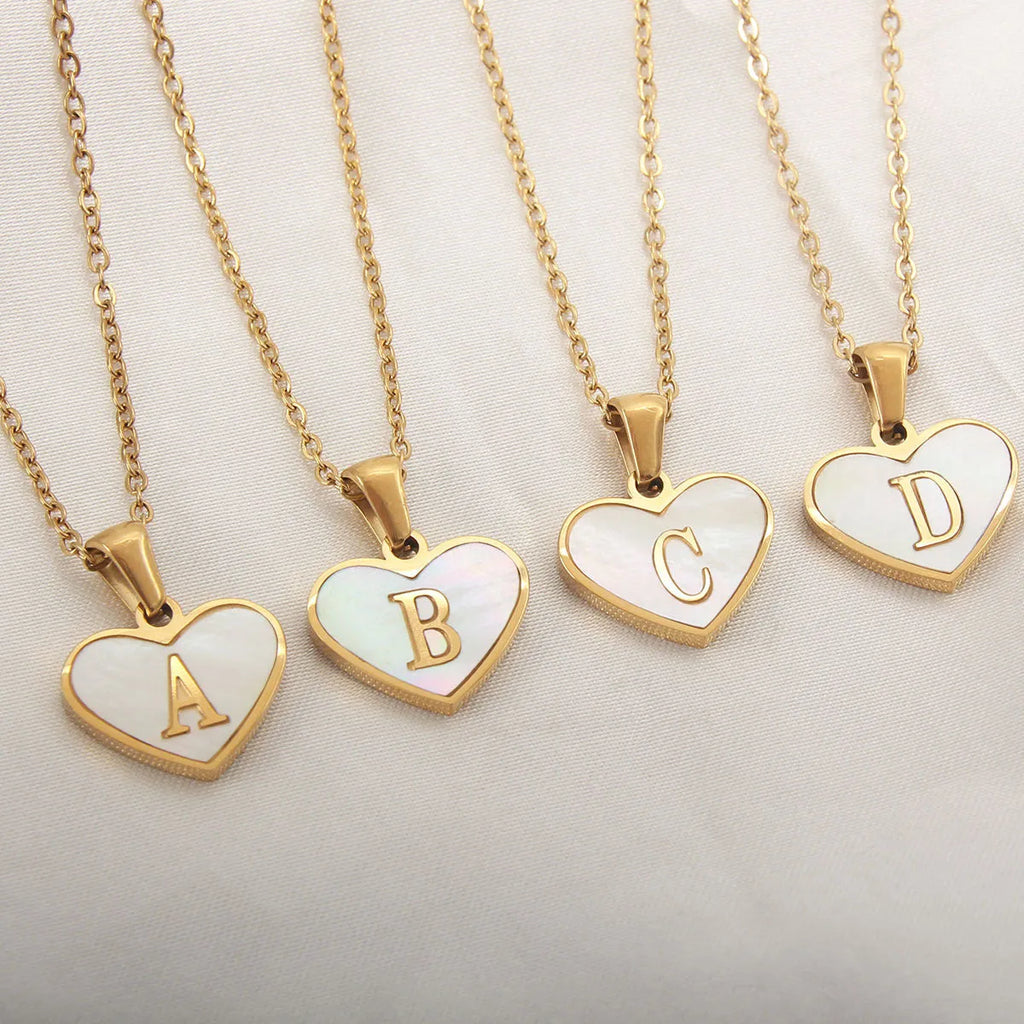 Gold-plated heart-shaped white shell initial necklace on a model, showing the adjustable clavicle chain.