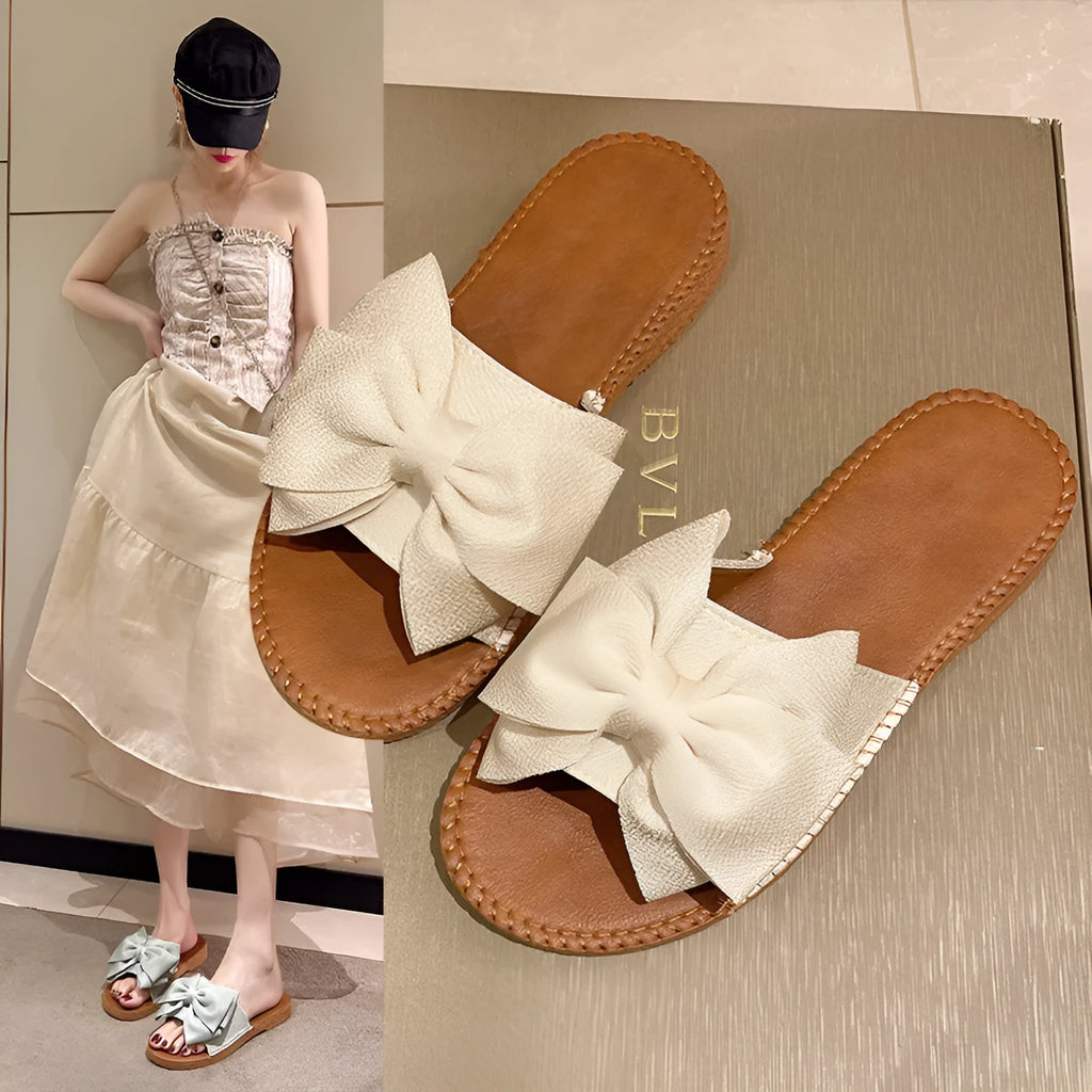 Women's beige suede slip-on sandals with a bow and soft rubber flat sole.