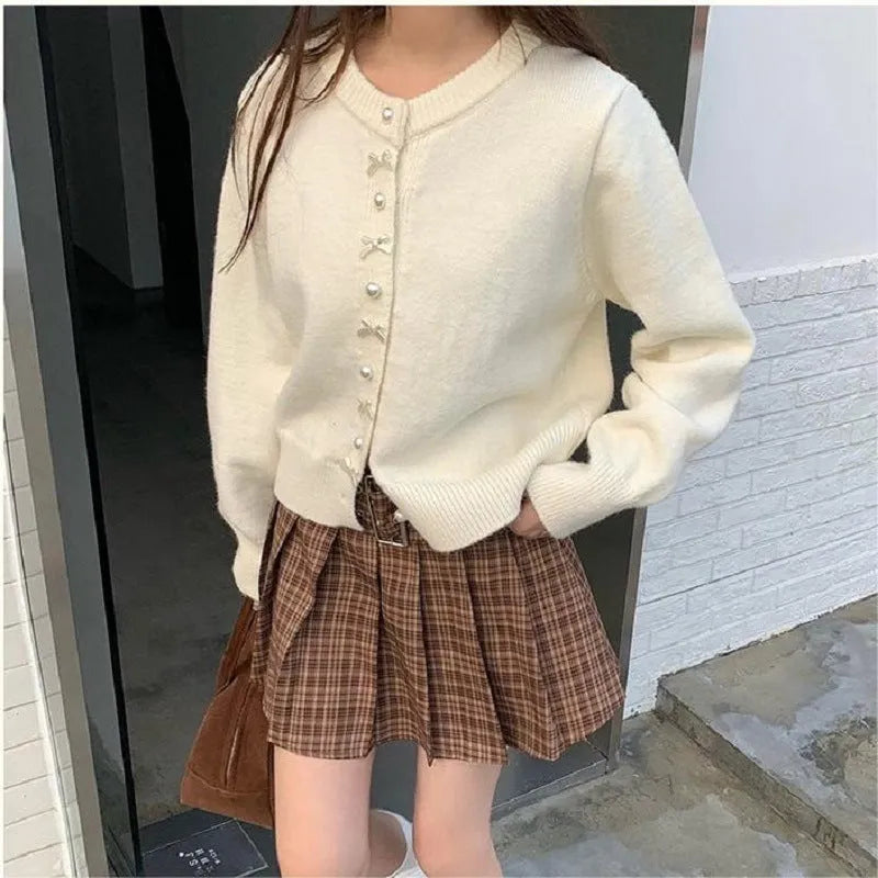 Women's solid colour cardigan with a front fabric bow and pearl button fastening, shown in a light colour.