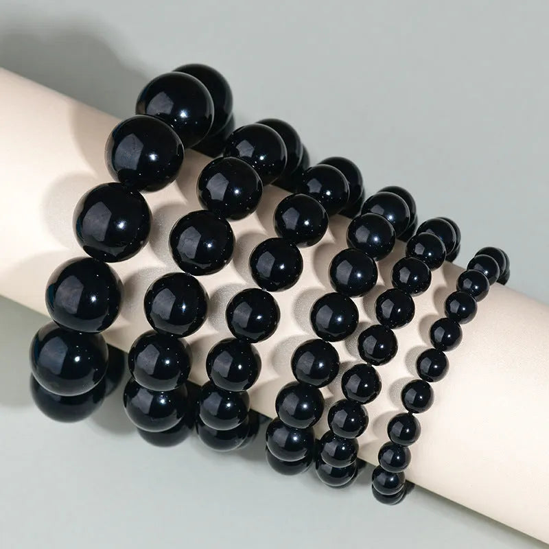 Hand-woven obsidian bracelet with round beads in adjustable sizes from 8mm to 16mm diameter, showing six colour options including black stone and rainbow eye obsidian.