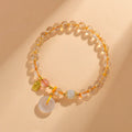 Gold rutilated quartz crystal bracelet with a safety buckle and a small rectangular blessing card pendant.