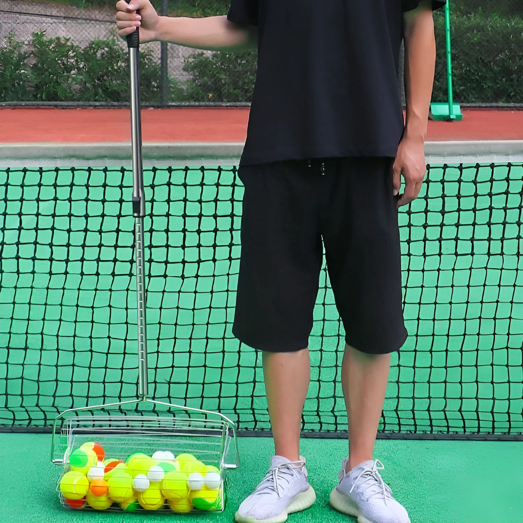 Stainless steel rolling tennis ball picker on a court, showing large adjustable frame.