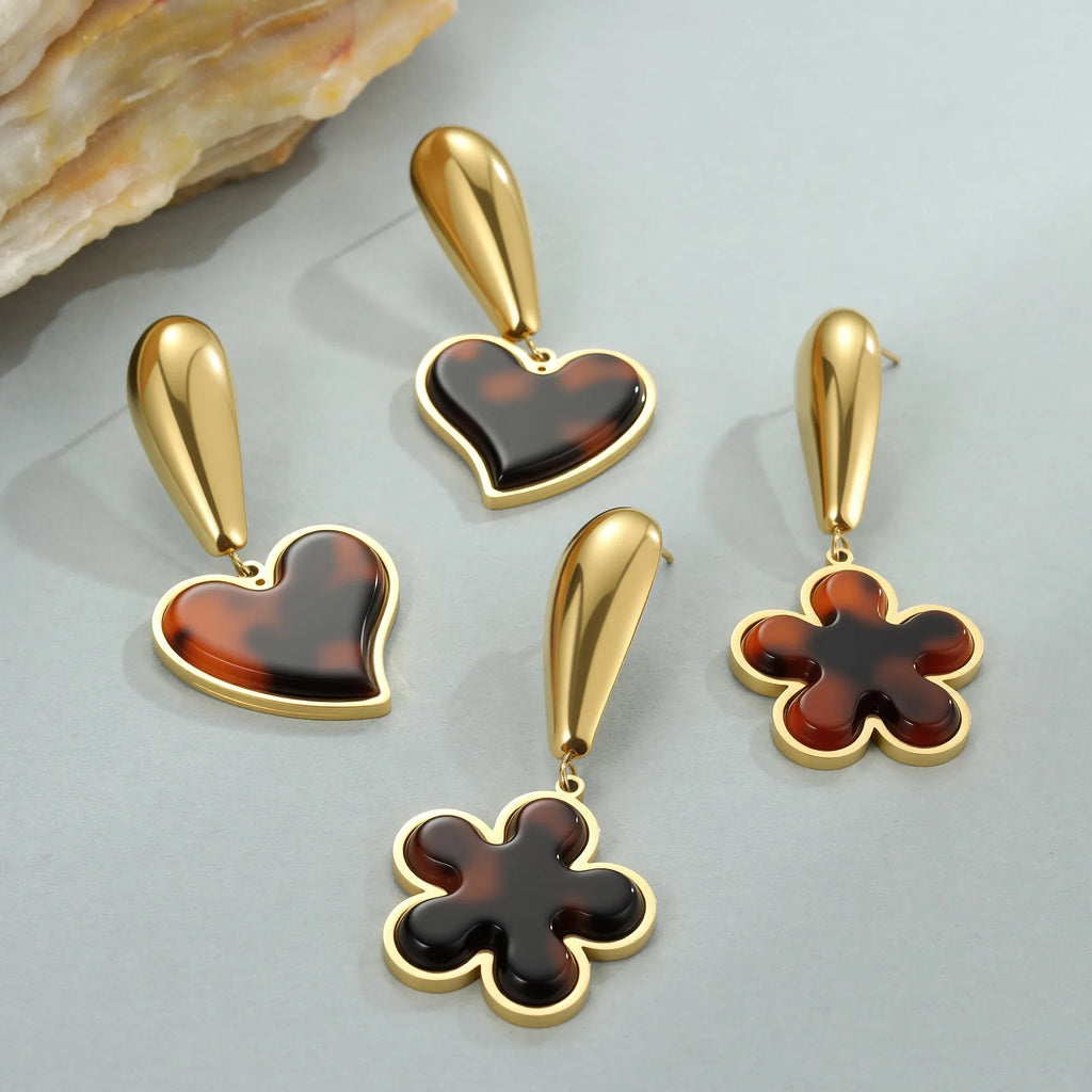 A pair of women's tortoiseshell resin earrings in hawksbill colour, showing heart-shaped and geometric flower designs on stainless steel with 18K plating.